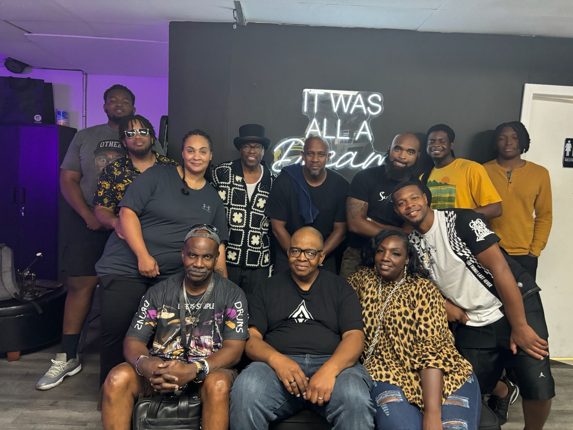 Group of people posing in front of a black wall with neon sign that says 