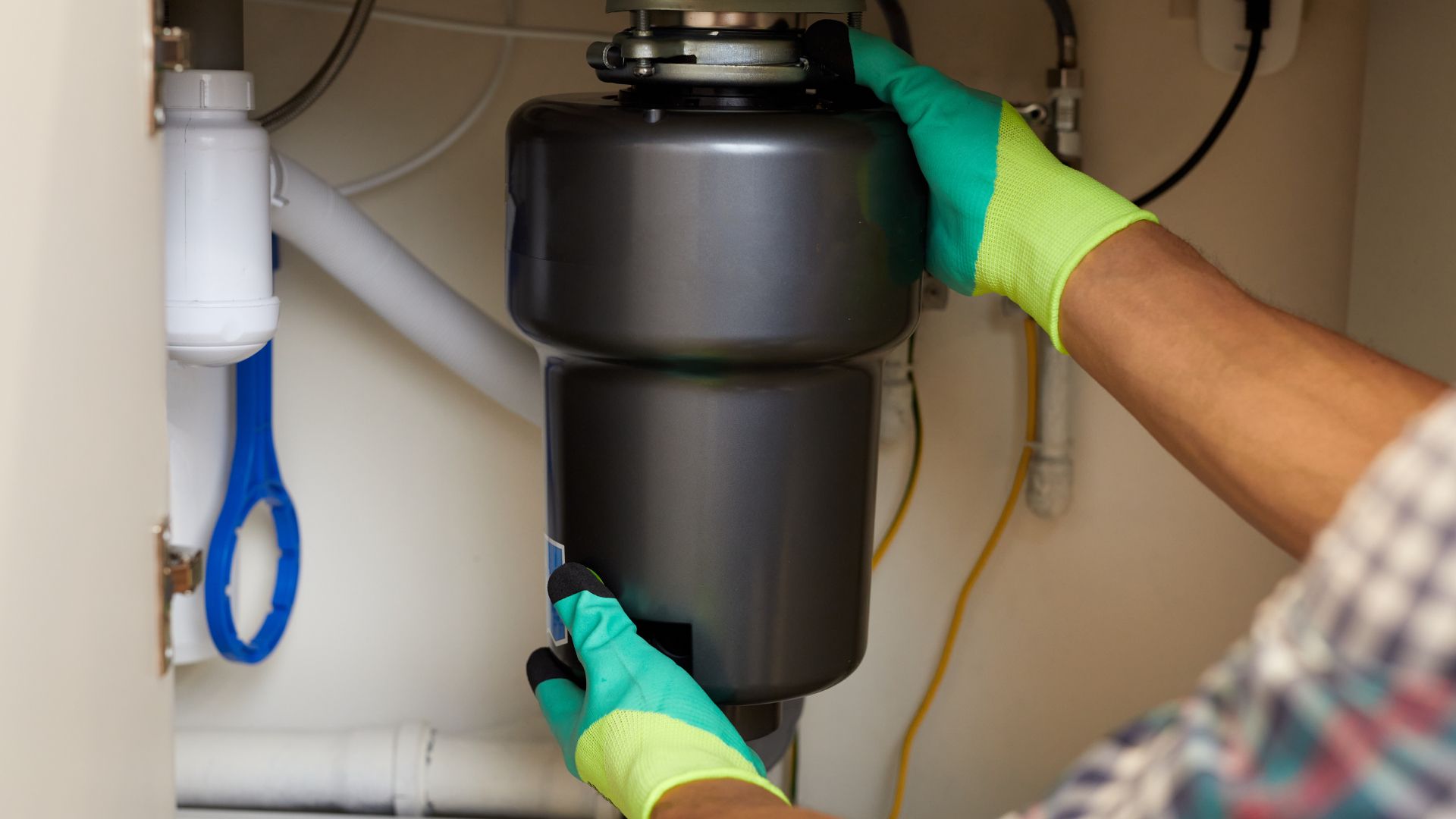 A person is fixing a garbage disposal under a sink.