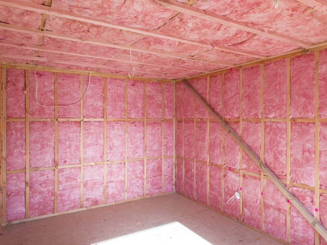 Pink insulation batts installed between wooden studs in a room's walls and ceiling.