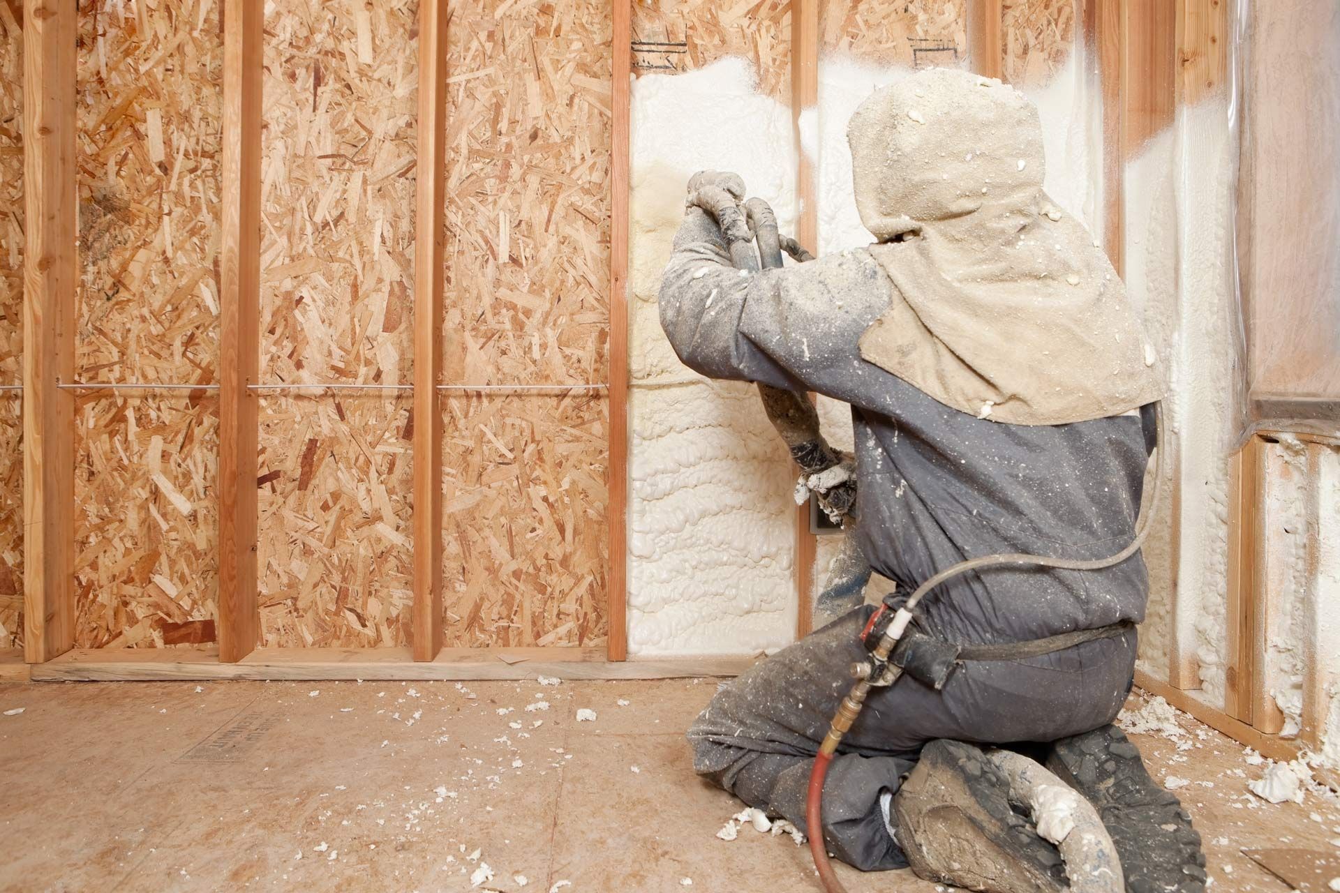 Worker spraying expandable foam insulation between wall studs for energy-efficient home insulation.