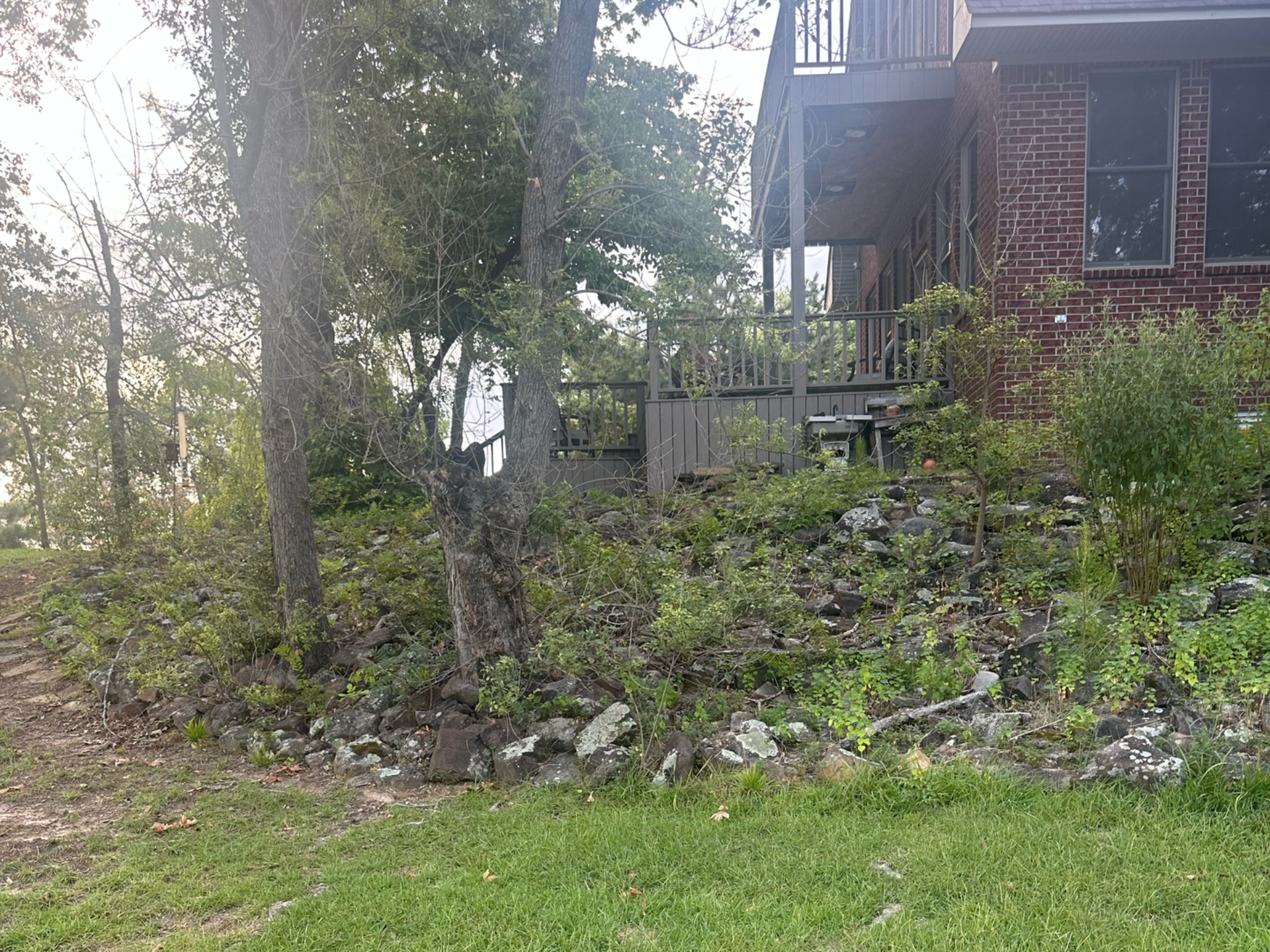 A brick house with a porch is nestled amongst trees and greenery.