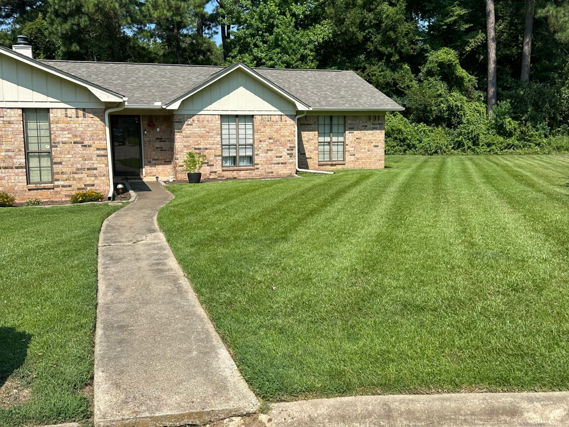 A brick house with a green lawn, a concrete path leading to the front door.