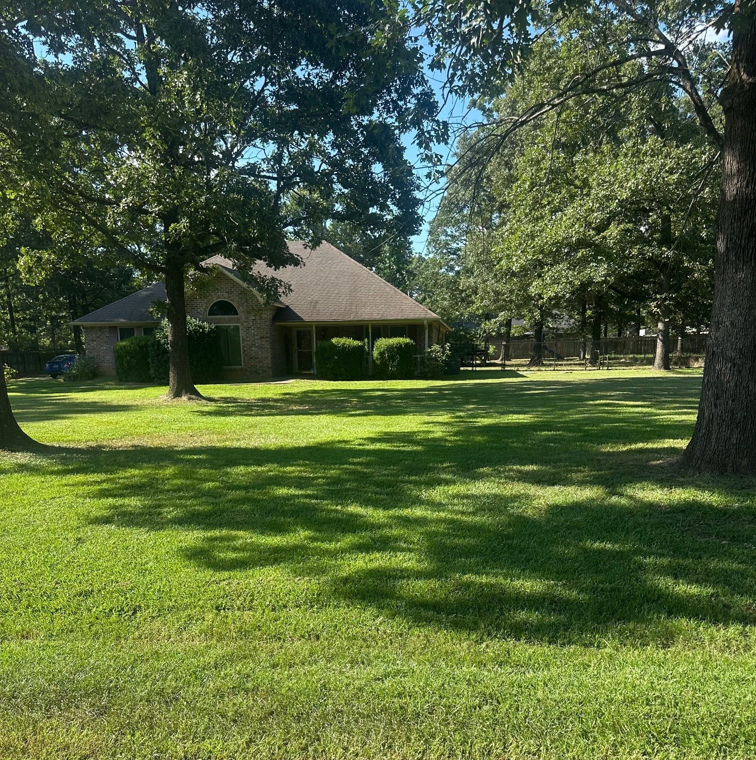 House with brick facade sits among large trees in a grassy yard.