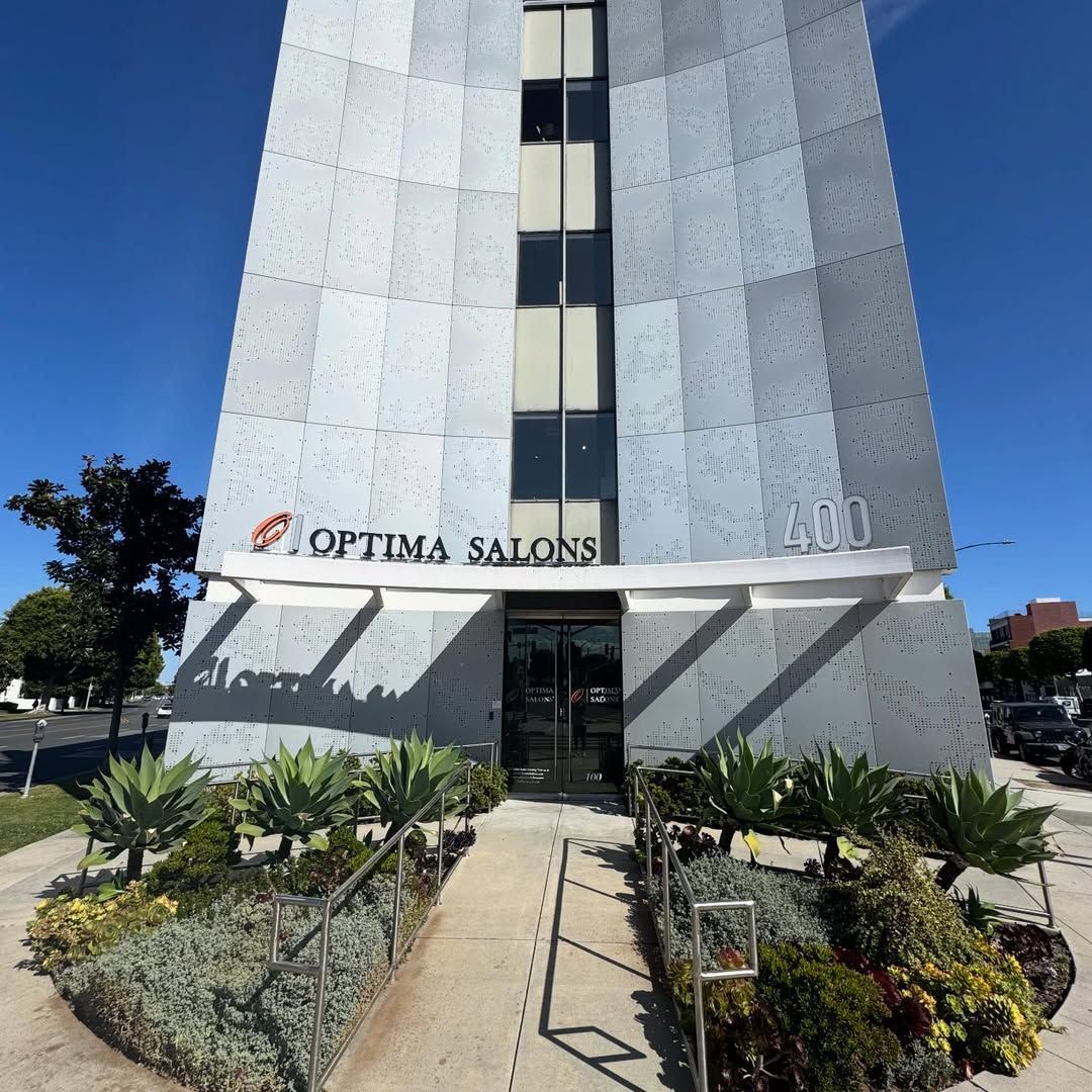 Optima Salons storefront in a tall white building with a glass entrance and landscaped walkway