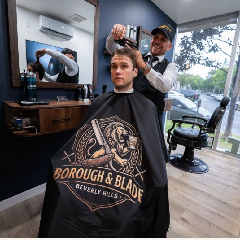Barber styling a seated customer wearing a black cape in a modern shop with window view