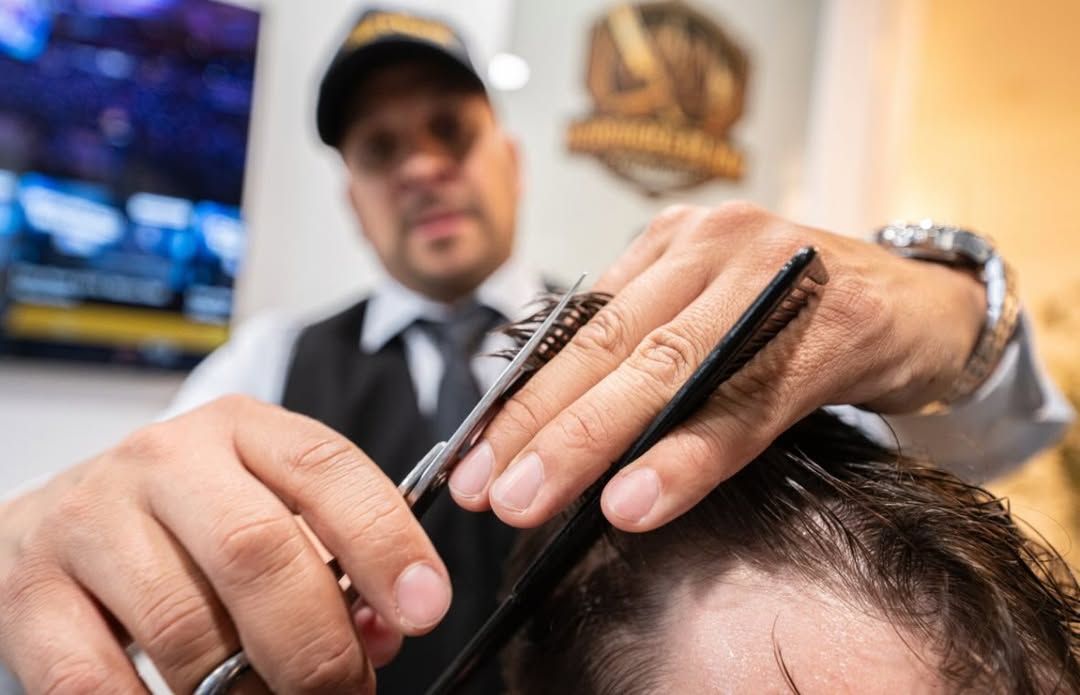 Barber trimming a customer’s hair with clippers in a salon, with a TV and wall decor in the background