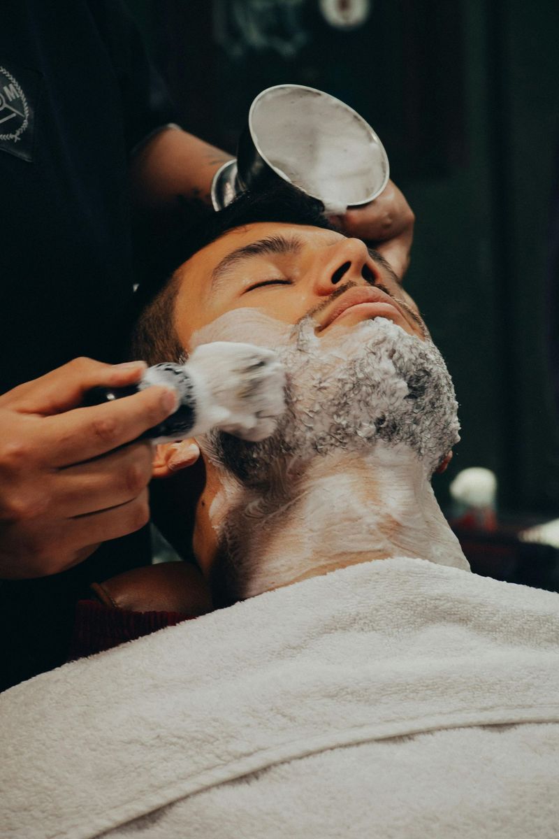 Barber shaving a reclining client’s face with lather and a straight razor in a close-up grooming scene