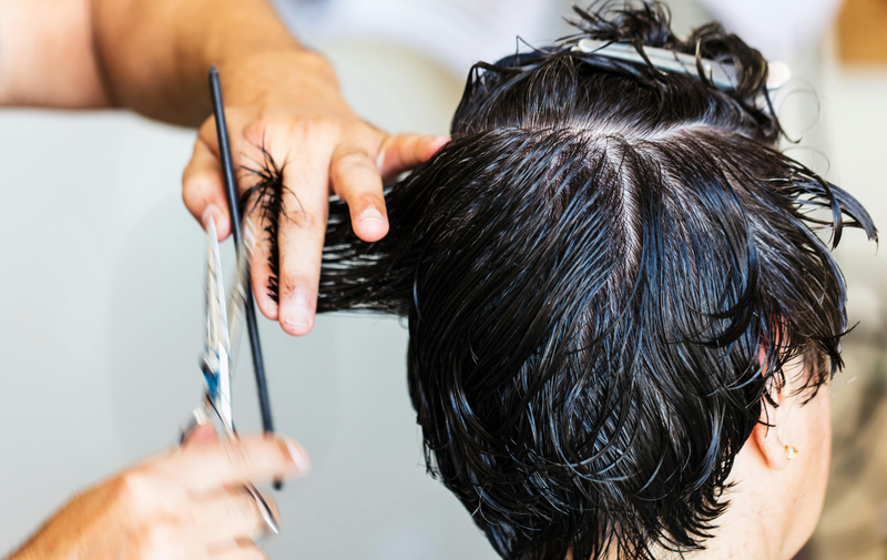 Hairdresser cutting wet dark hair with scissors and comb during a salon haircut