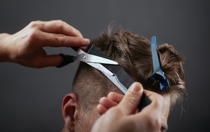 Barber cutting a man's hair with scissors and a comb, close-up in a salon