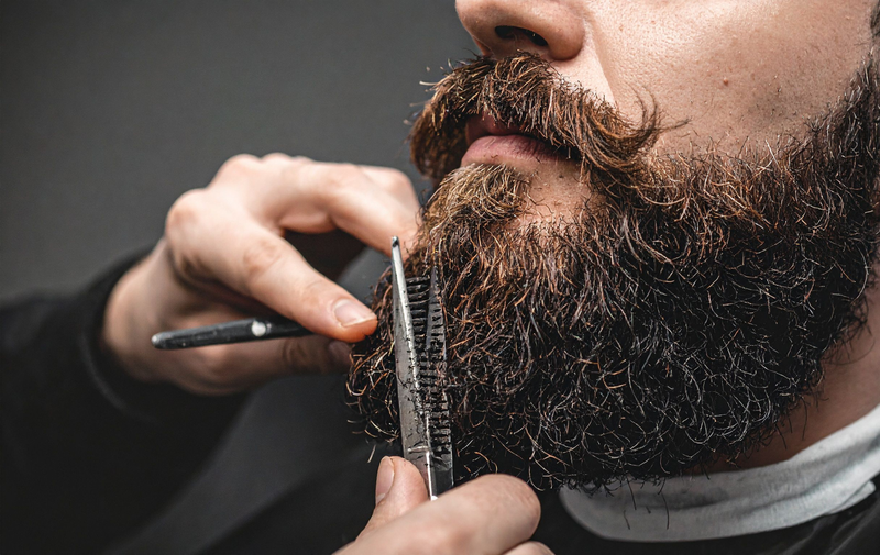 Barber trimming a thick brown beard with scissors and comb in a close-up shot