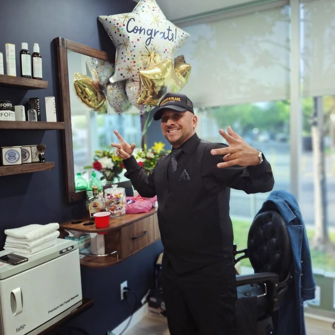 Man posing in a salon with balloons, making hand gestures and smiling near a chair and styling station
