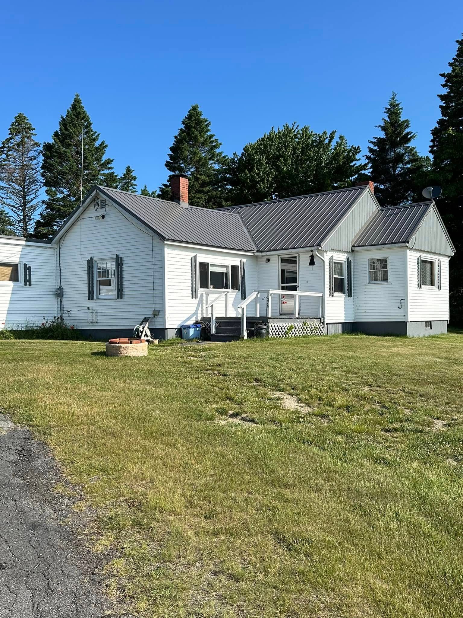 White house with black roof, green shutters, grass yard, and blue sky.