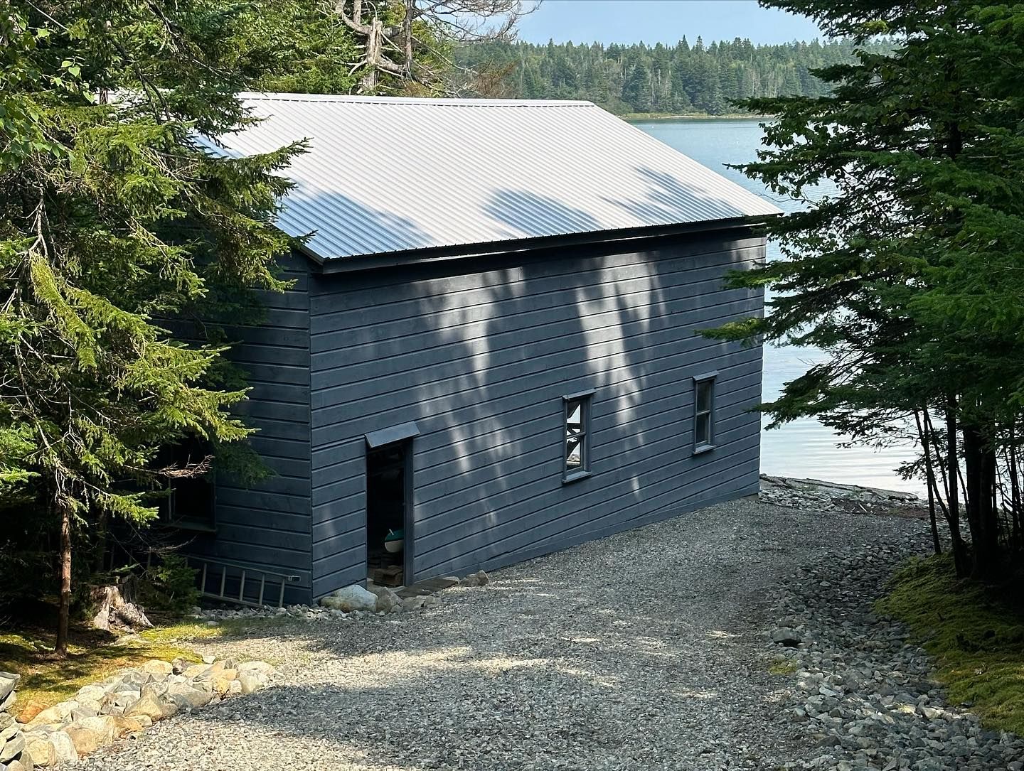 Gray building with white roof, featuring numerous holes. Situated by water, trees surround.
