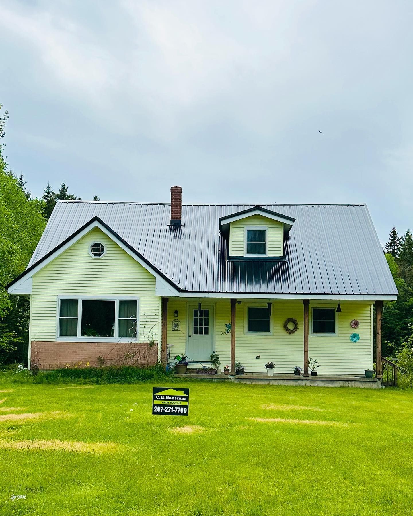 Yellow house with metal roof, small porch, and dormer window, set on a green lawn.