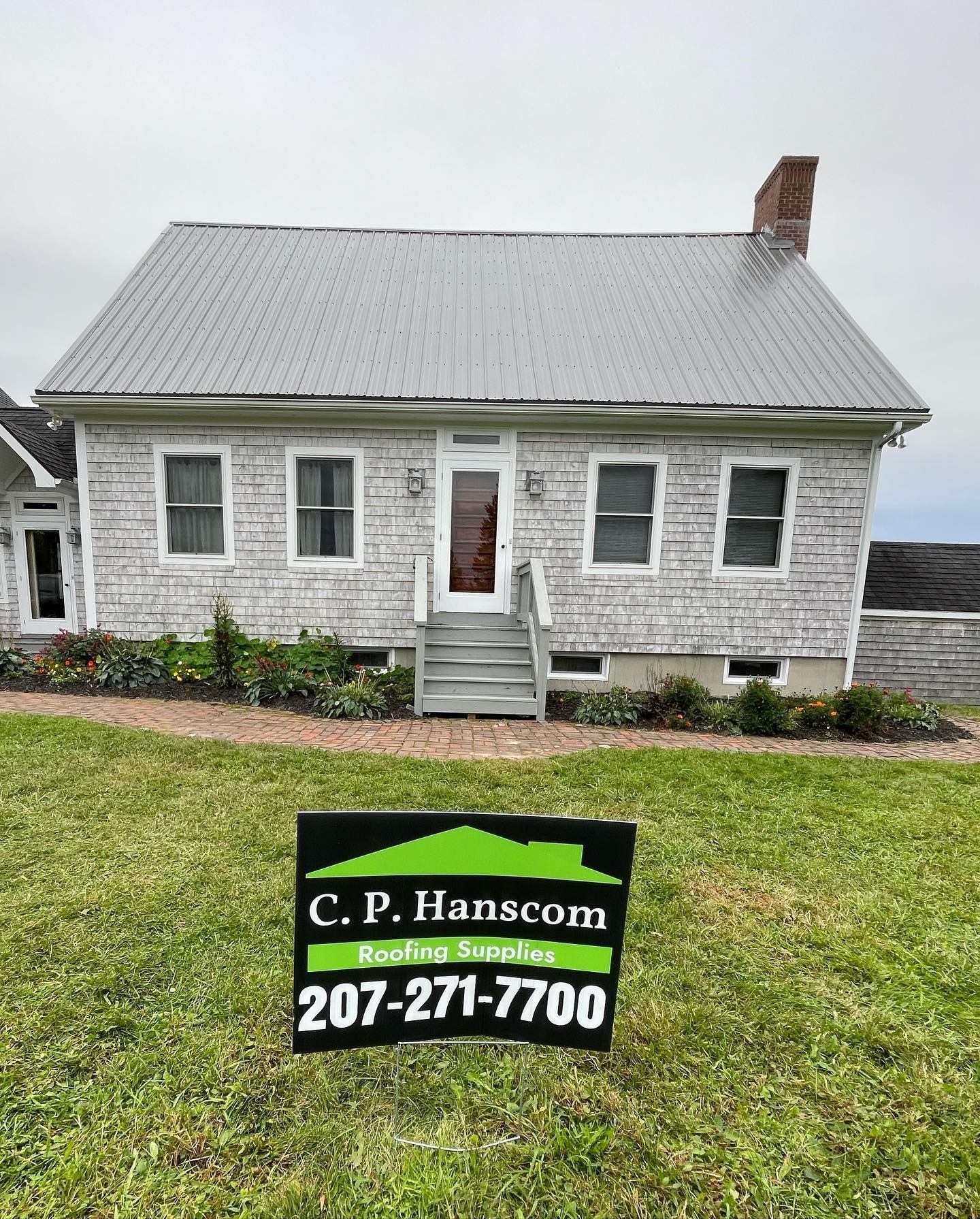 Small white house with a metal roof and a real estate sign in front.