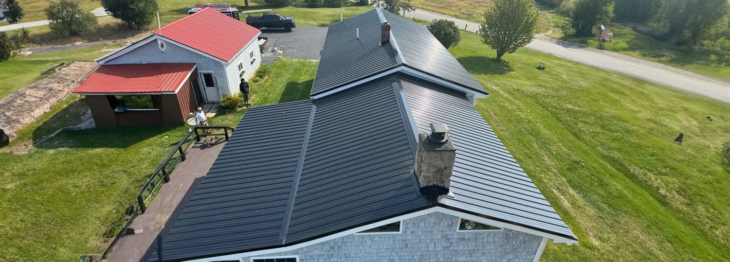 Aerial view of two houses with red and dark gray roofs on a grassy lot.