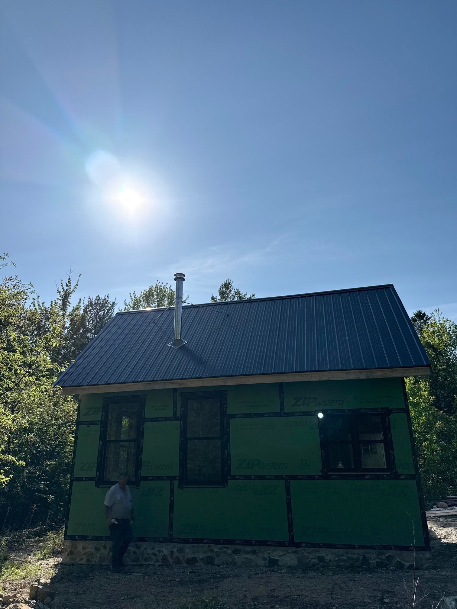 Small unfinished cabin with blue roof and green siding under a sunny sky.