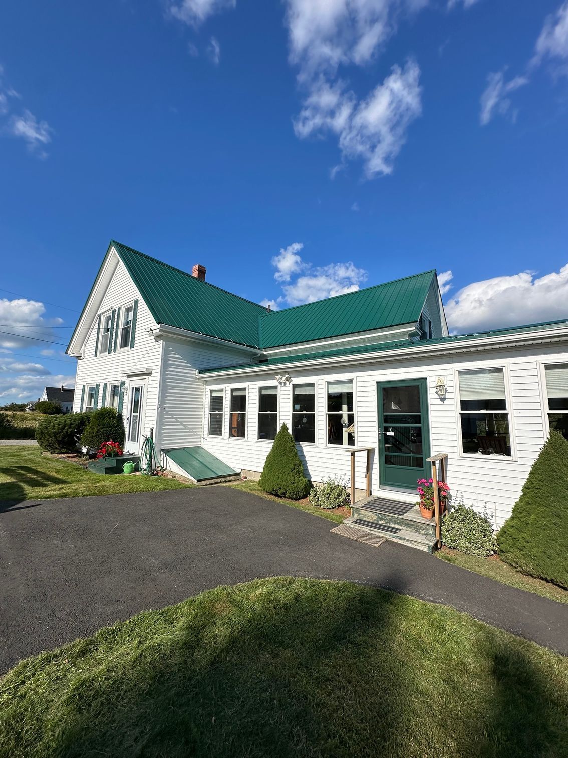 White building with green roof, windows, and door, sitting on grass, with a blue sky.