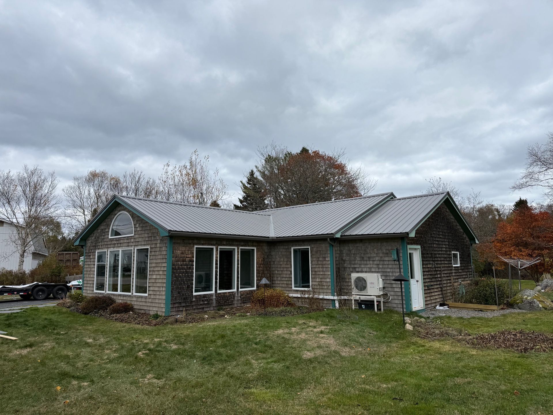 House with wood siding and metal roof on a grassy lot under an overcast sky.