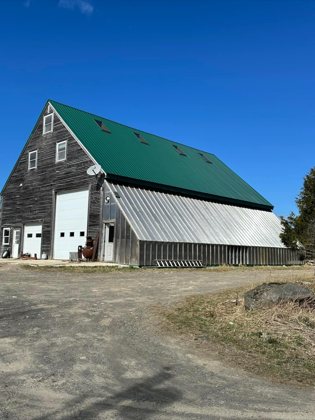Large barn with green roof and metal siding against a blue sky.