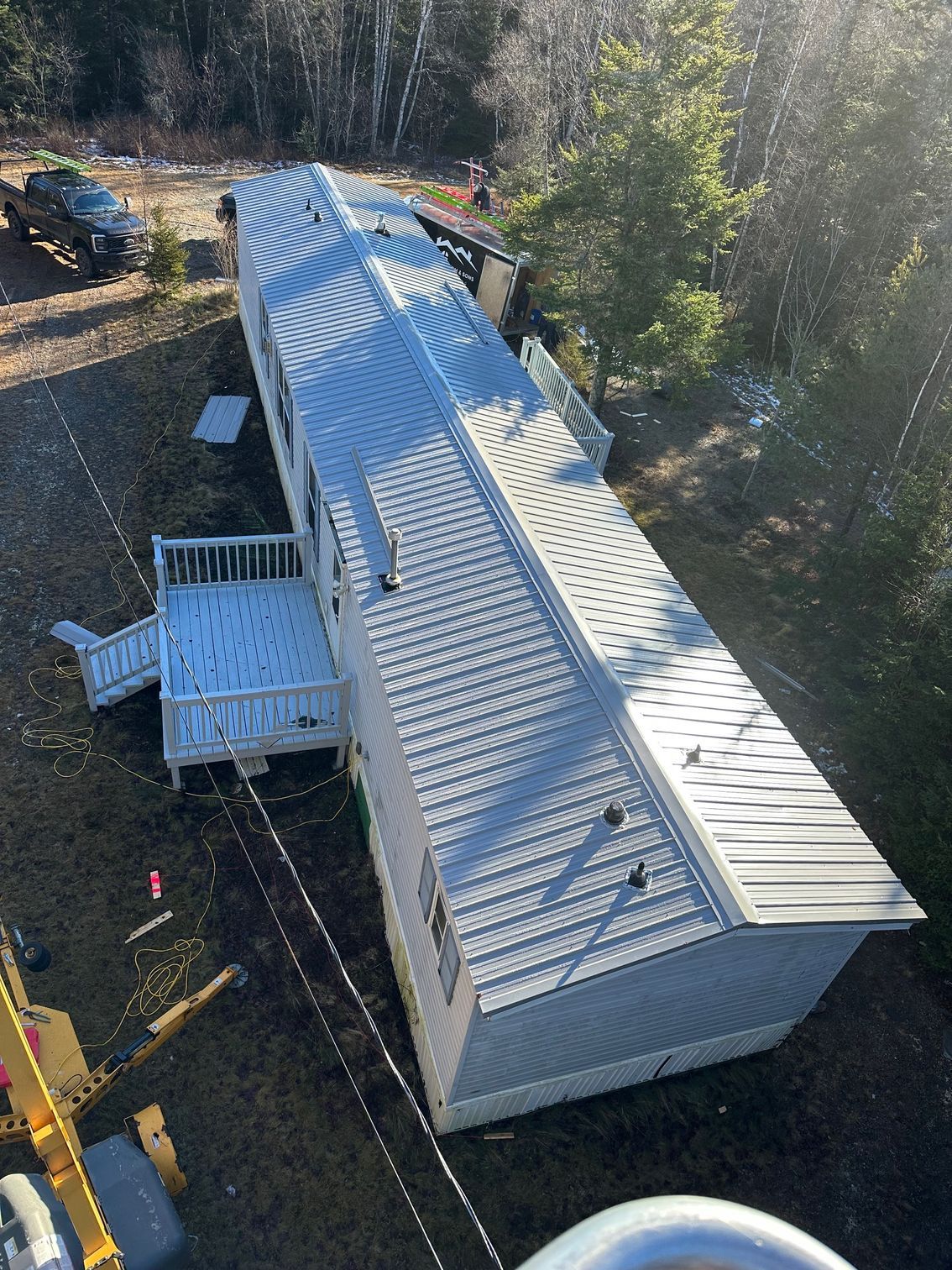 Long, light-gray house with a white deck, surrounded by grass and trees under a sunny sky.