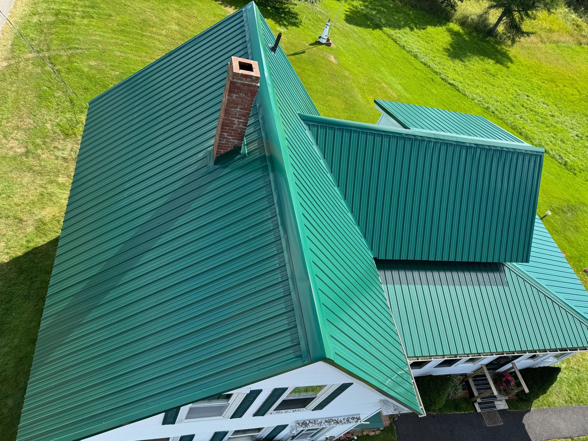 Green metal roof on a white house with a brick chimney, seen from above.