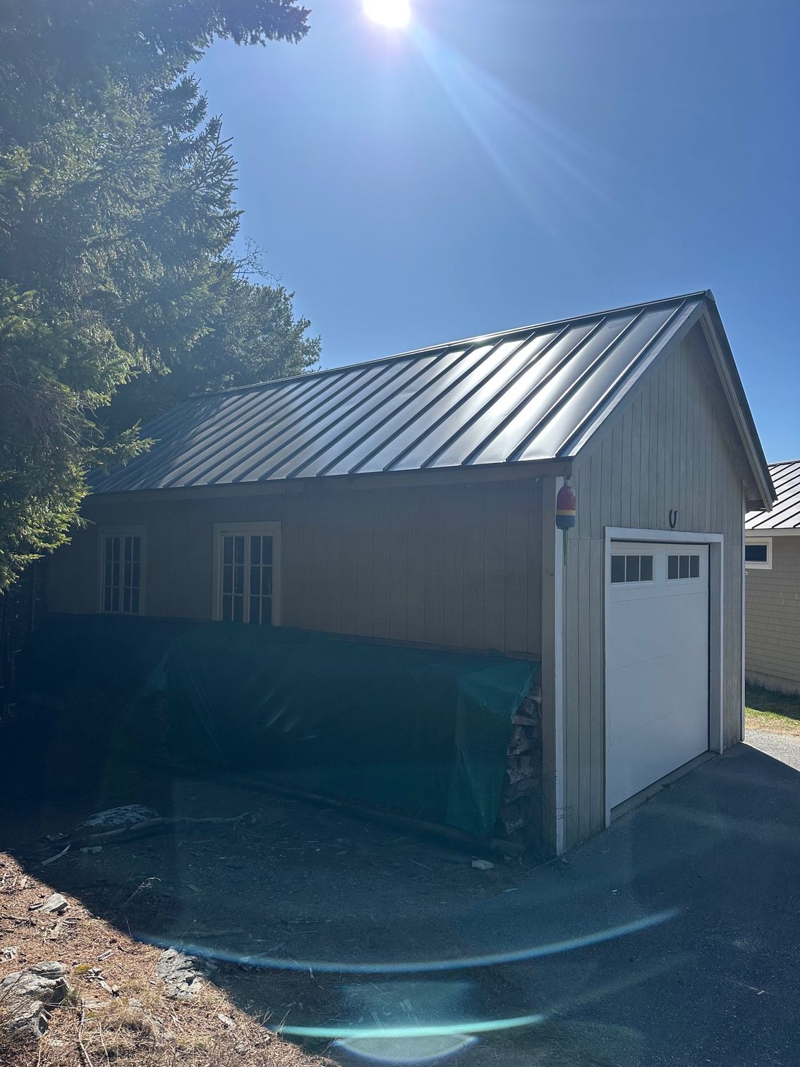 Garage with metal roof on a sunny day. White garage door, two windows, and dark-colored driveway.