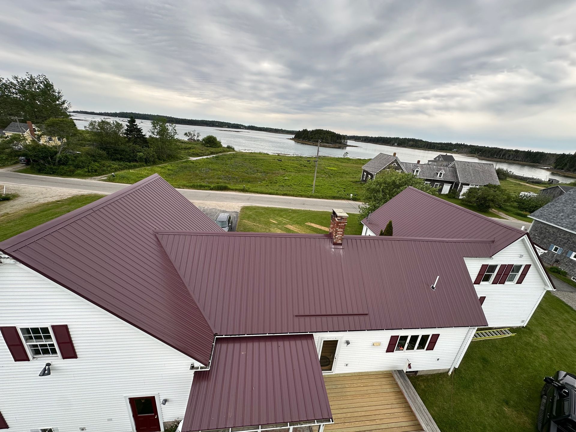 White house with maroon roof overlooking a body of water and green landscape under a cloudy sky.