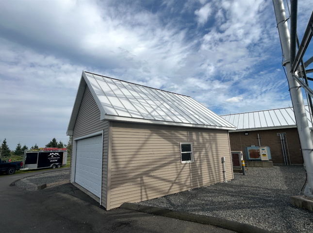 Tan building with a white garage door, metal roof, and a clear sky with clouds.