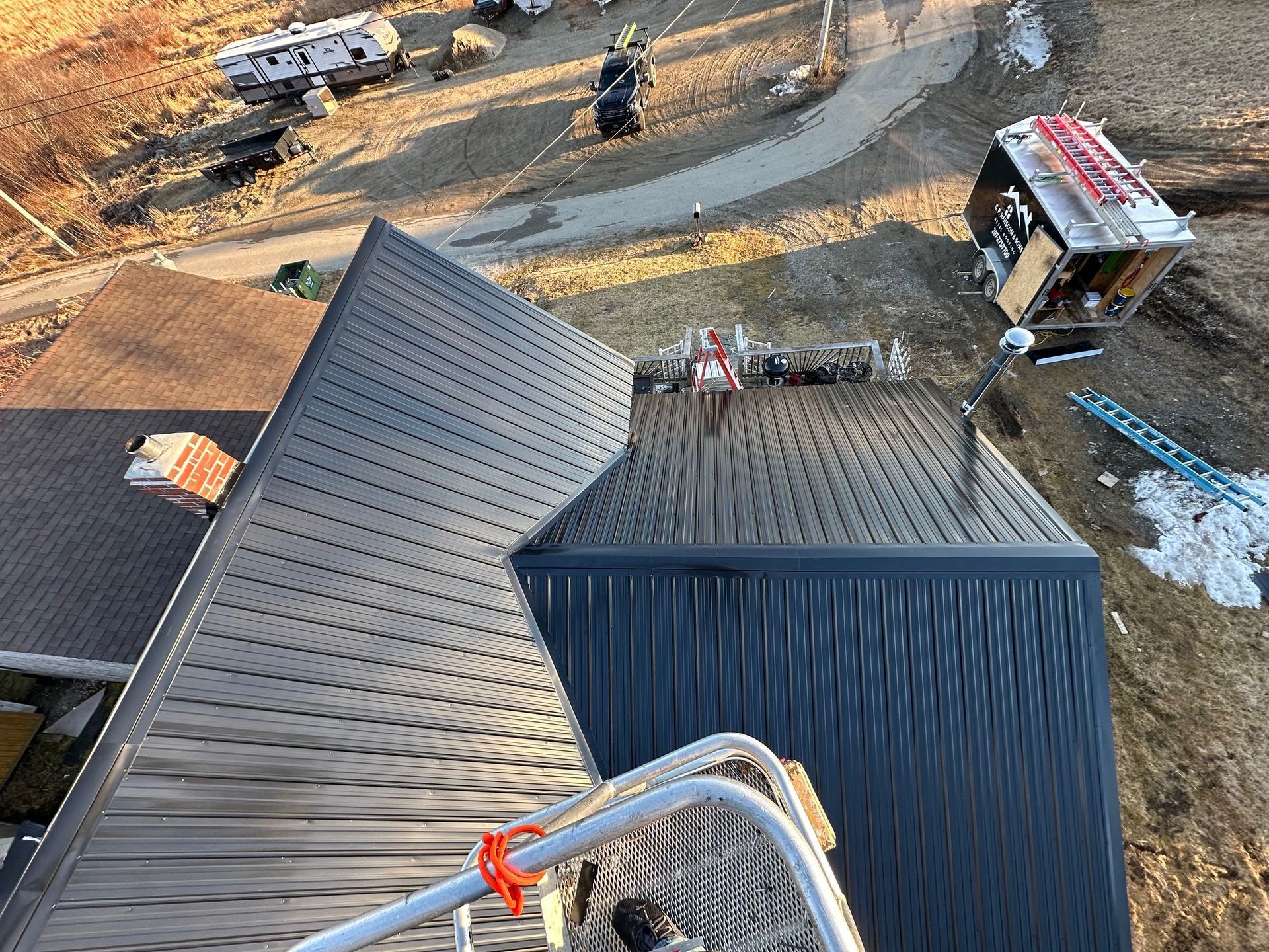 Dark metal roof with chimney, construction site in the background, daytime.