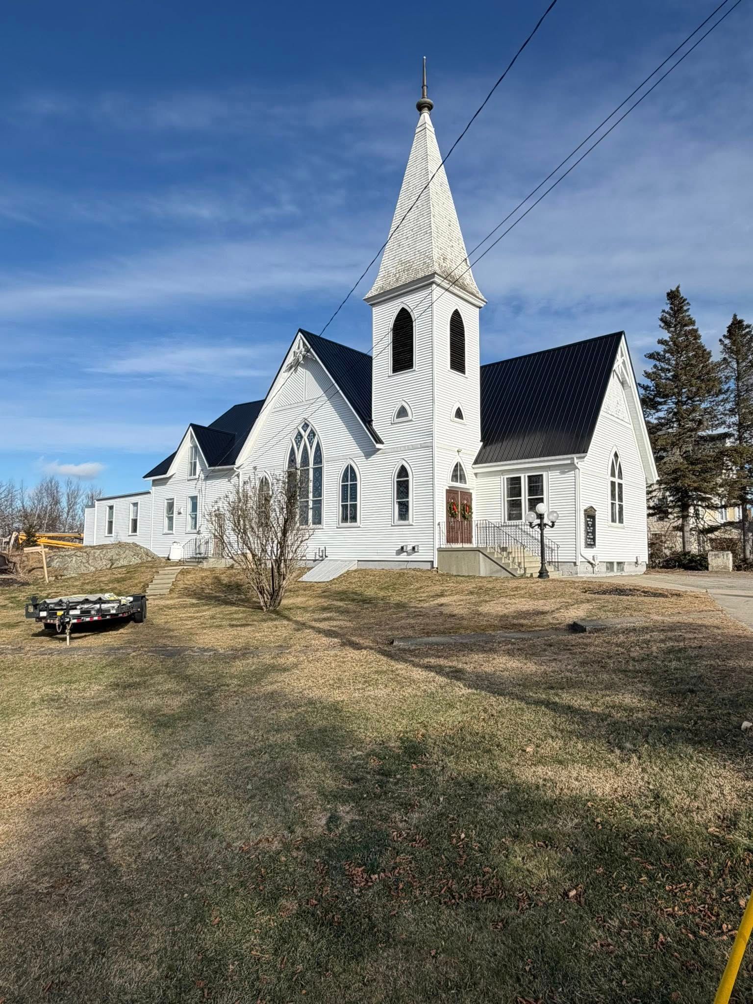 White church with tall steeple against a blue sky, brown grass in the foreground.