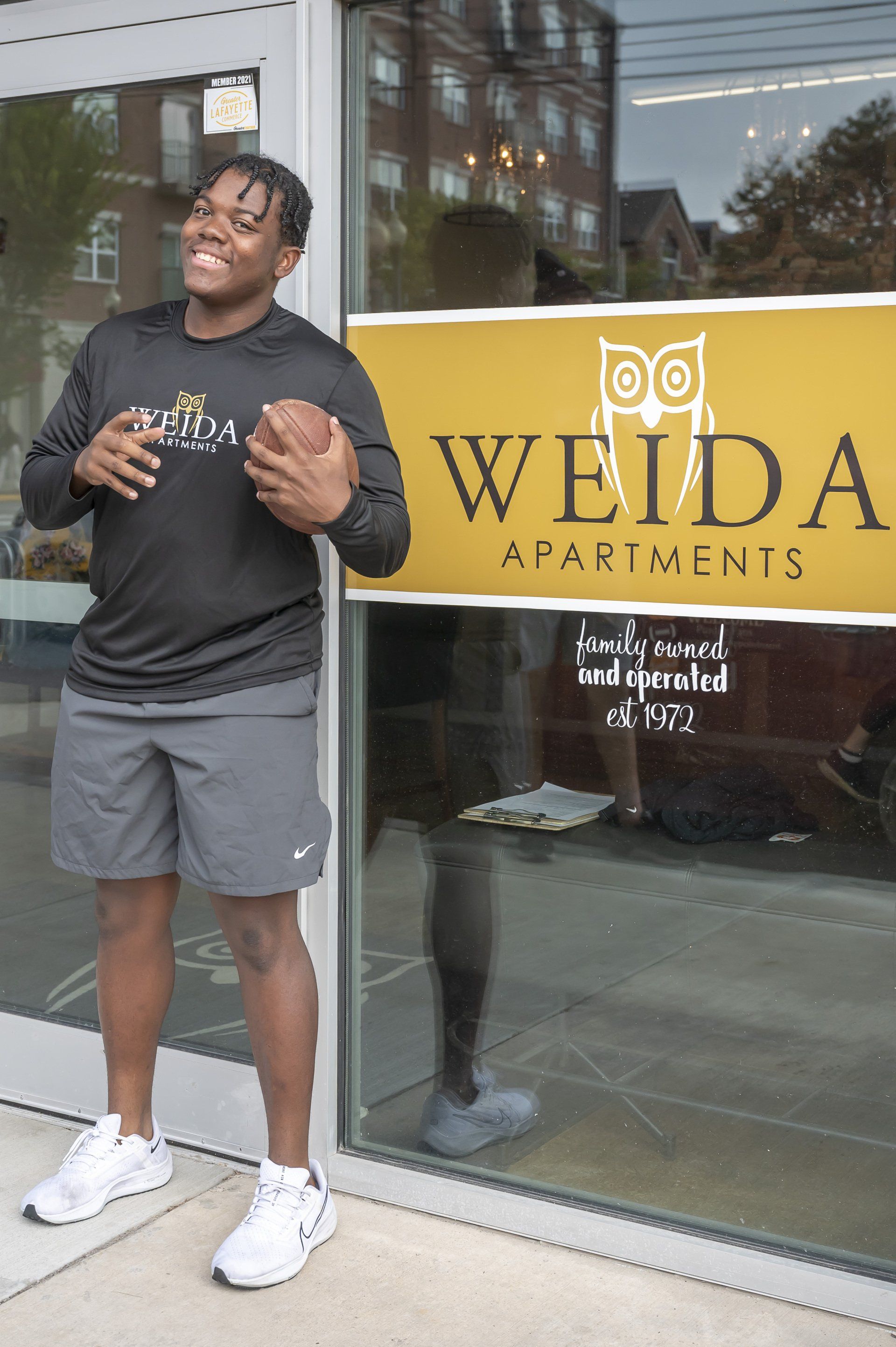 Purdue student holding football in front of Weida office front entrance.