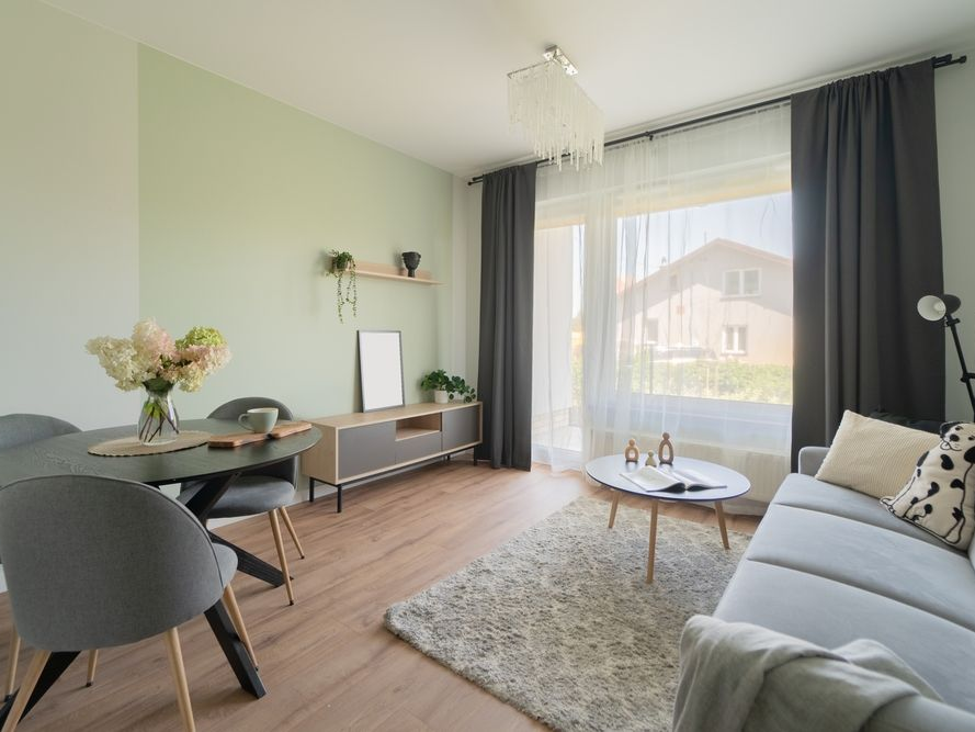 Living area in a modern apartment. A sofa is central, with an adjacent dining zone and balcony access. European residential interior with open layout, parquet floors, and contemporary design solutions