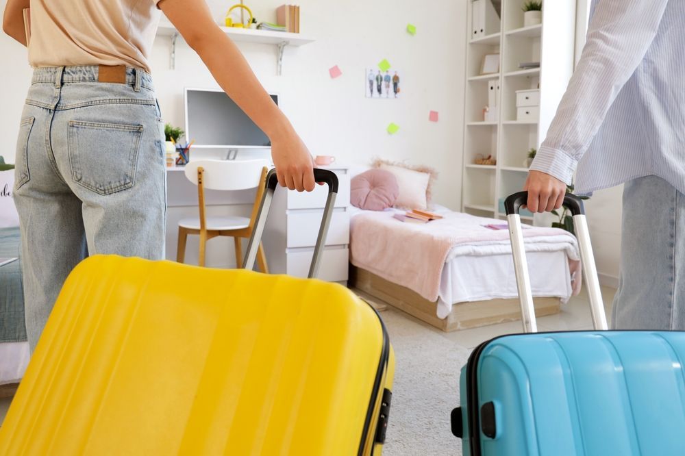 Female students with suitcases in a room on moving day, back view