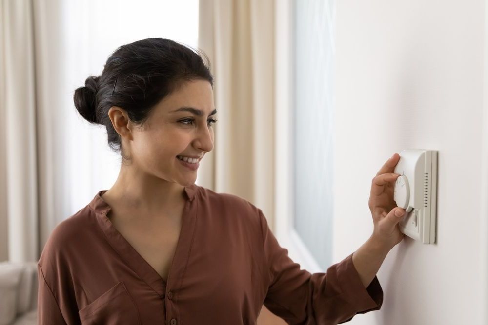 college aged woman setting her apartment thermostat