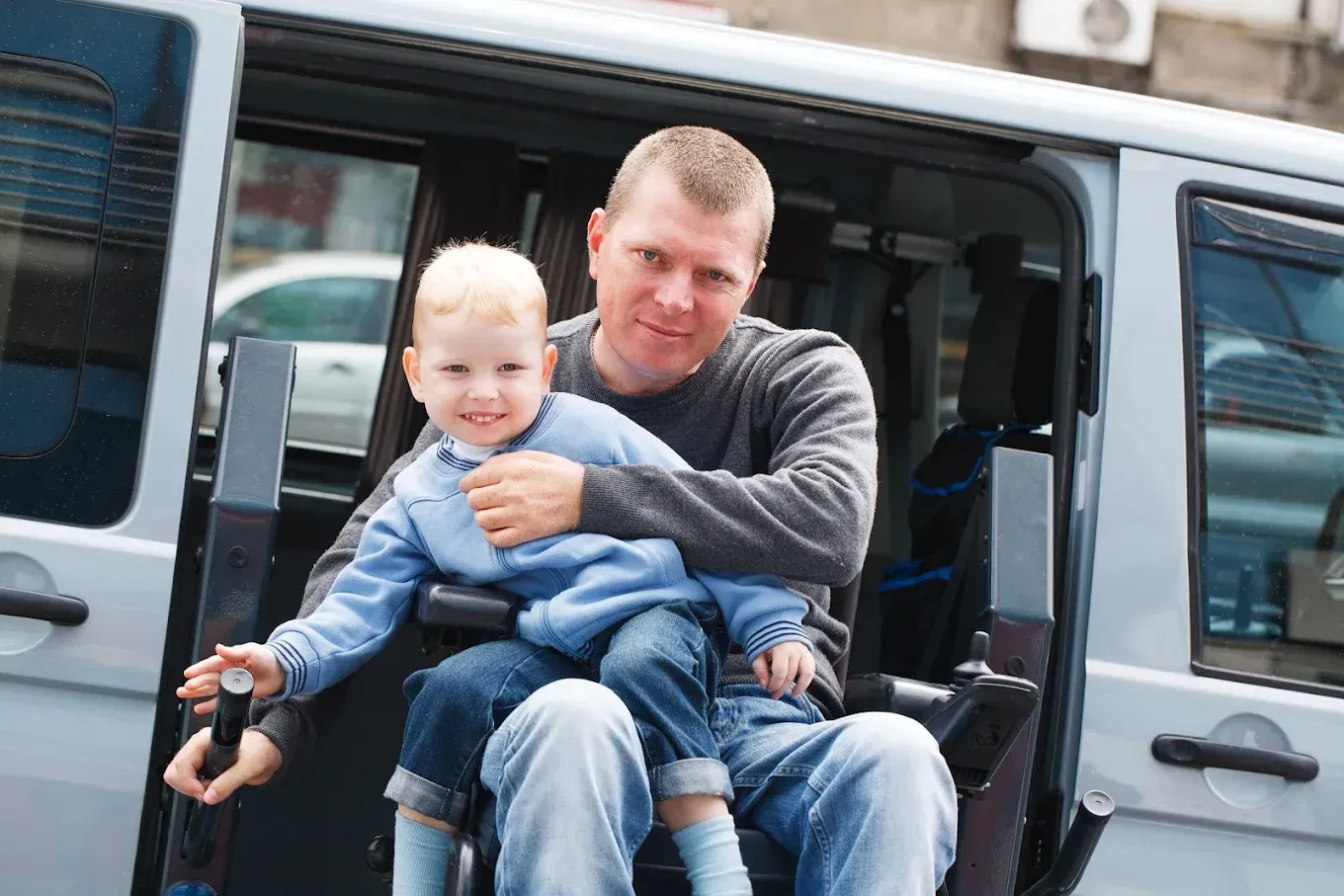 Man and child in a wheelchair accessible van; man is holding the child, both smiling.