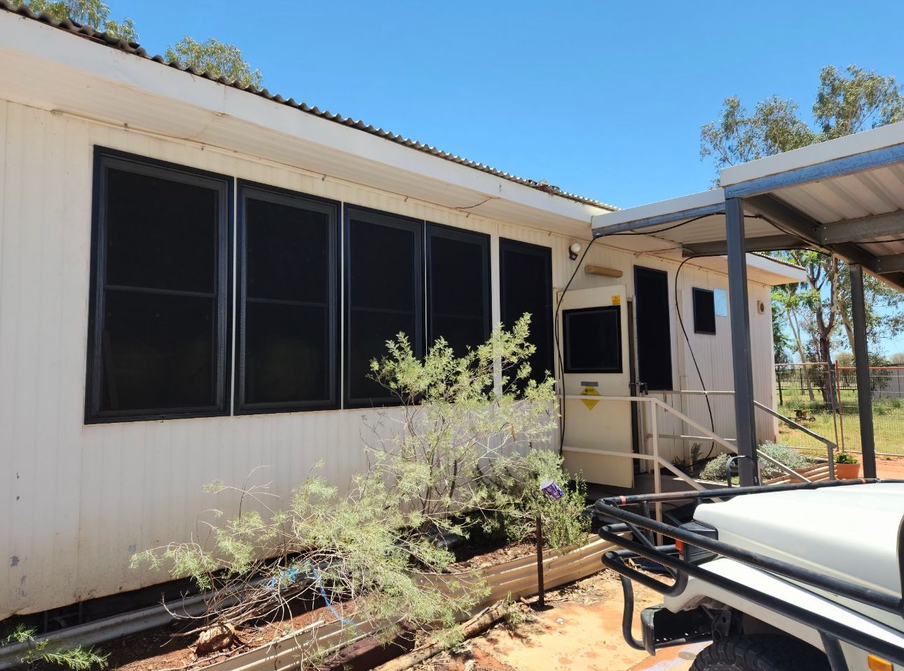 A white modular building with dark-screened windows and a small covered entry, set against a clear blue sky.