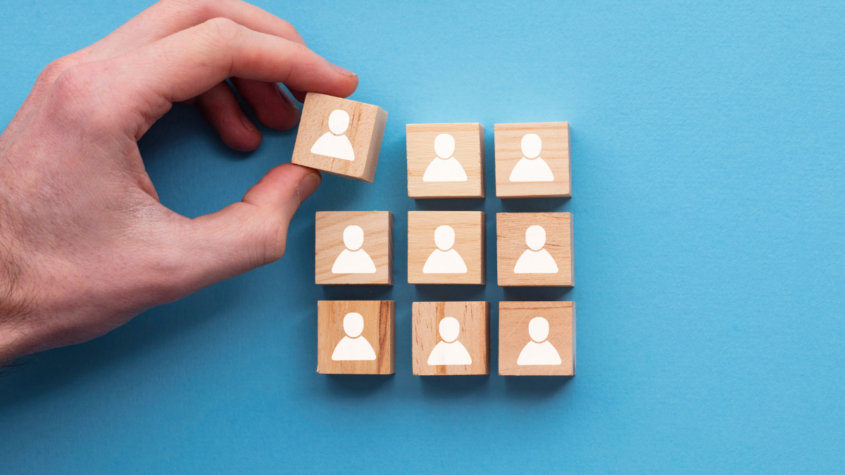 9 small wooden blocks with a single person icon printed on each, with one of the wooden blocks held by a person's hand