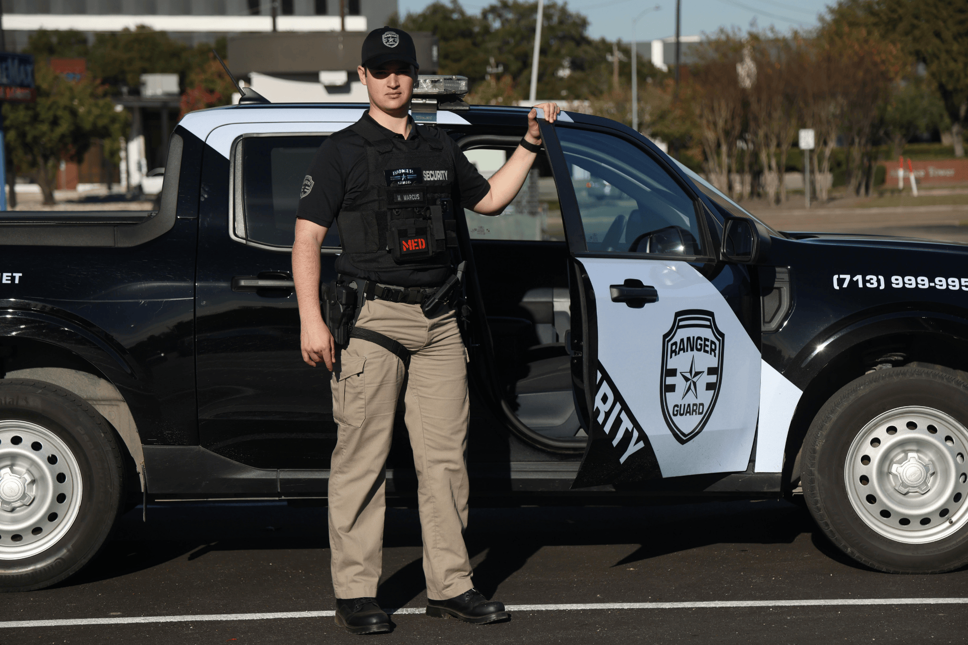 Security guard standing beside a marked patrol vehicle with the door open, ready for mobile security patrol and rapid response in a commercial area.