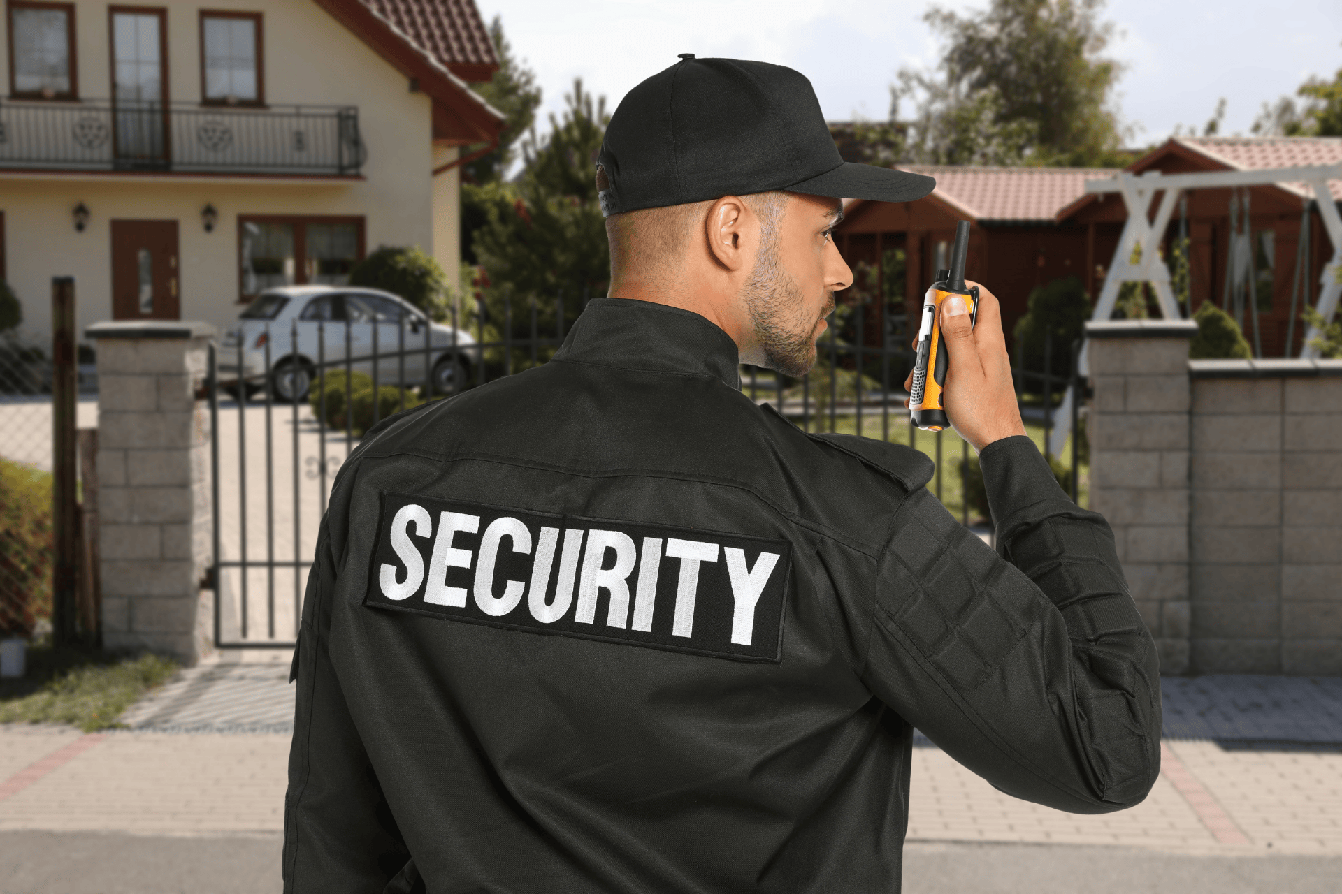 Security guard speaking into a radio while patrolling outside a gated residential property, monitoring the neighborhood.
