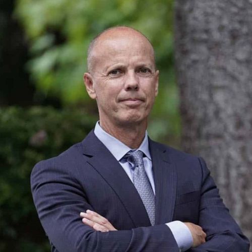 A man in a suit and tie is standing with his arms crossed.