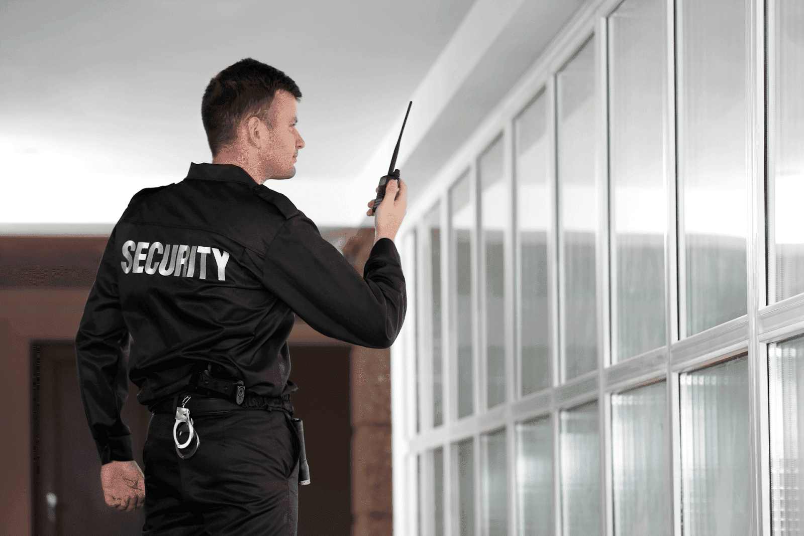 Security guard holding a walkie-talkie while patrolling a building corridor.