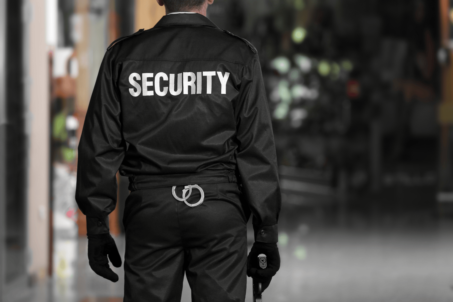 Security guard in uniform walking indoors with ‘SECURITY’ printed on the back of their jacket.