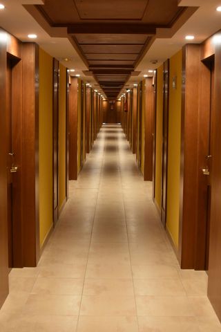 Long hotel hallway with wooden doors and ceiling, yellow walls, and tiled floor.