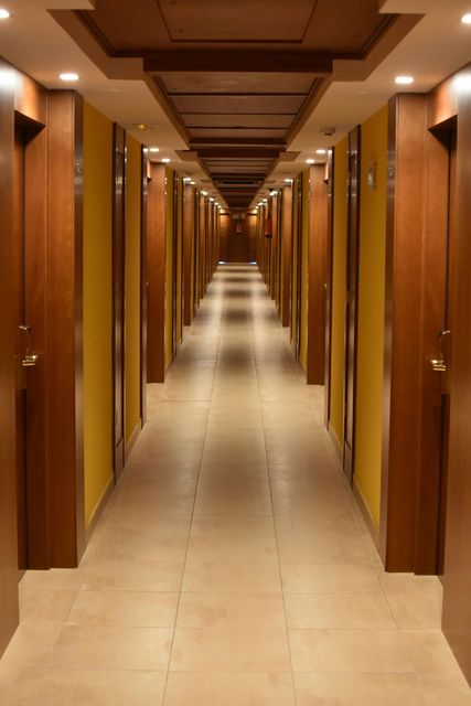 Long hotel hallway with wooden doors and ceiling, yellow walls, and tiled floor.