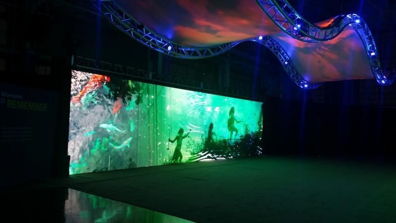 A large screen is hanging from the ceiling in a dark room.