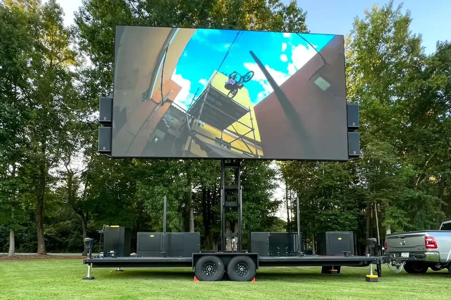 A large screen is on a trailer in a grassy field