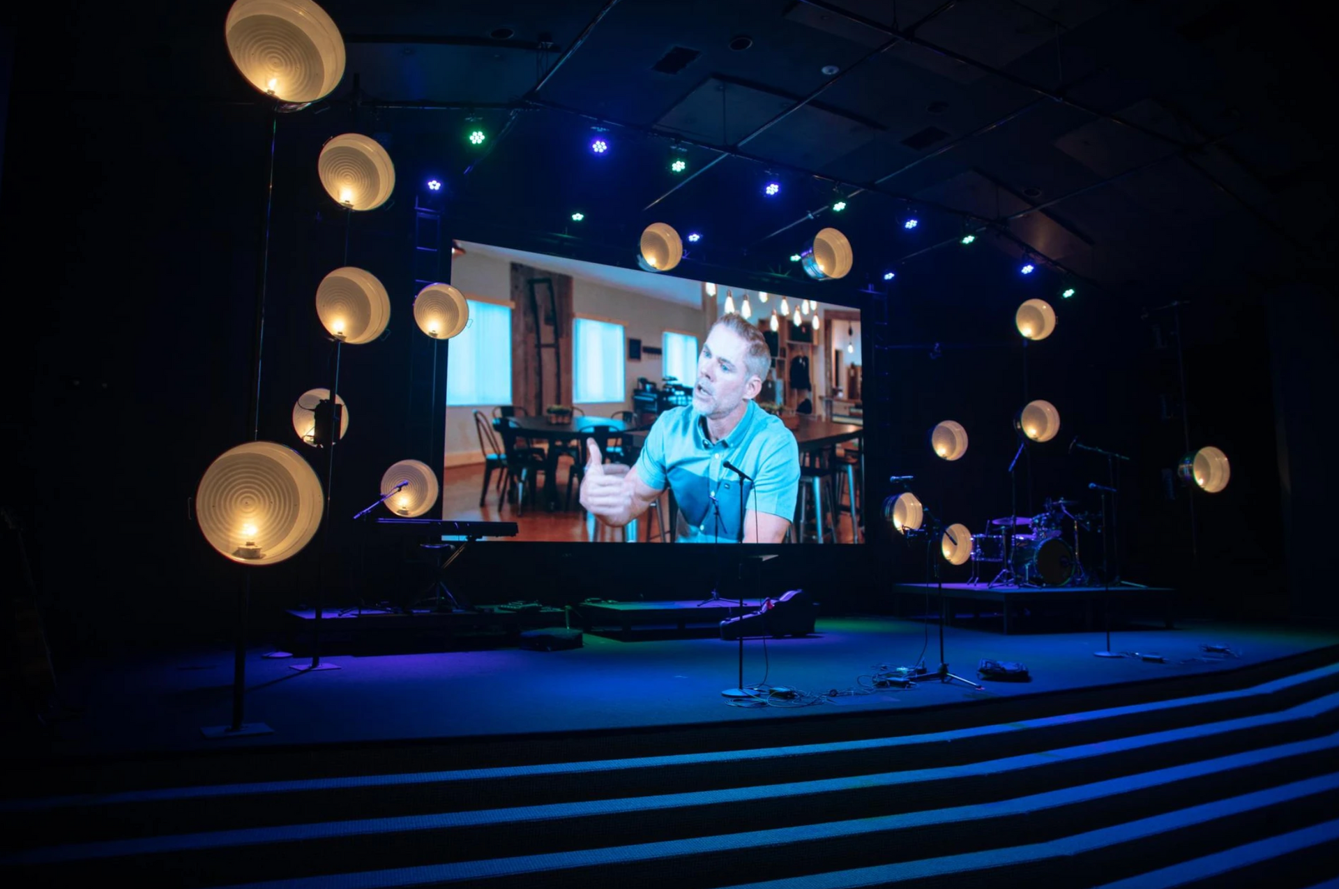 A man is sitting in front of a large screen on a stage.