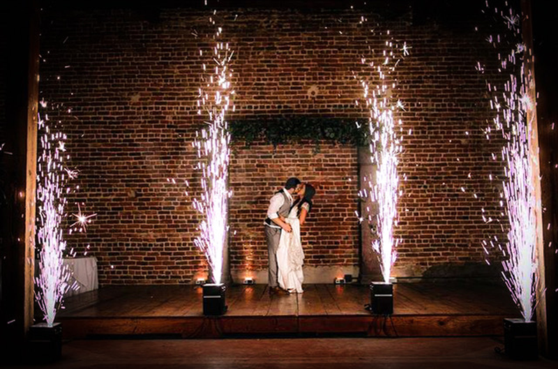 A bride and groom are kissing on a stage in front of sparklers.