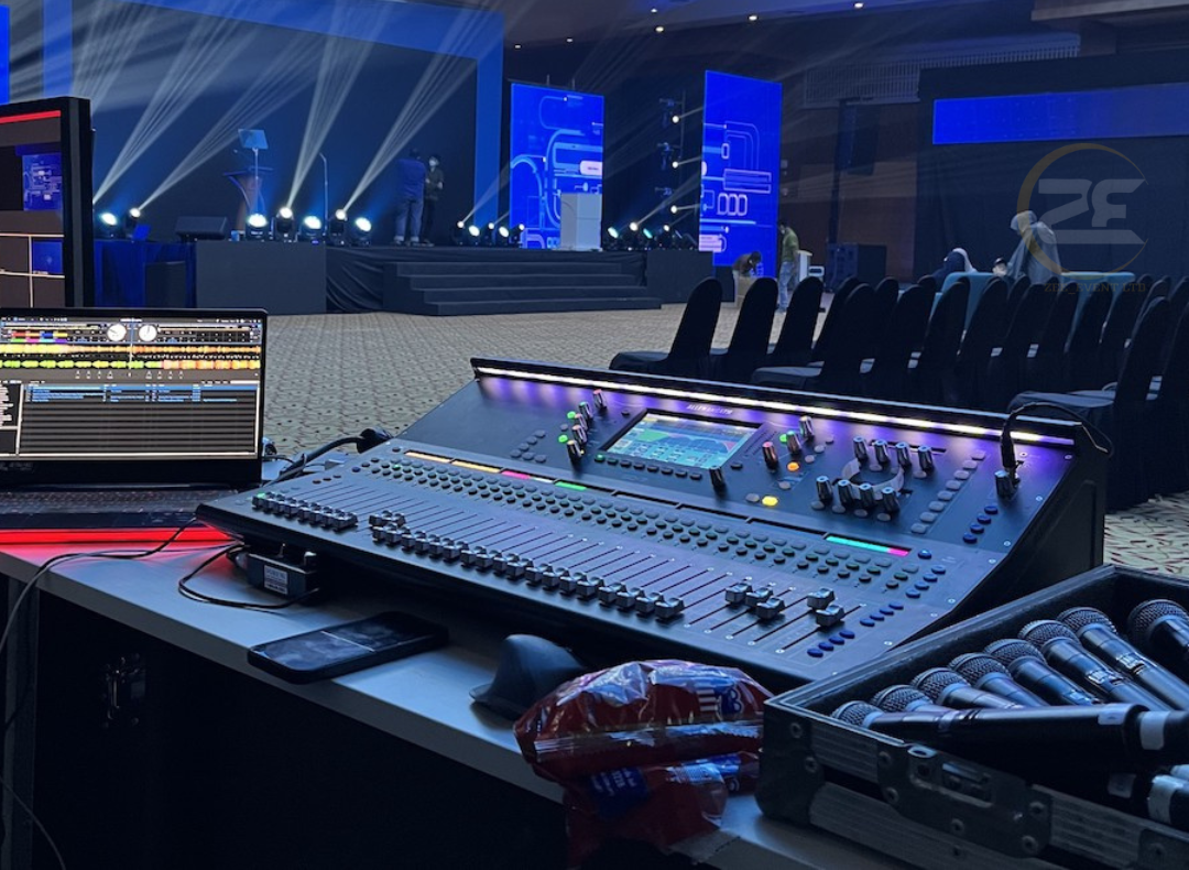 A mixer is sitting on a table in front of a stage.